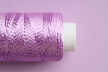 Spool of sewing thread on violet background, closeup. Space for text