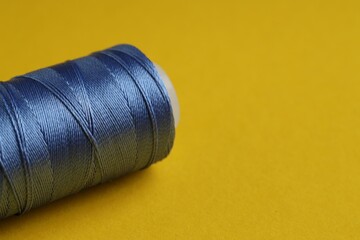 Spool of blue sewing thread on yellow background, closeup. Space for text