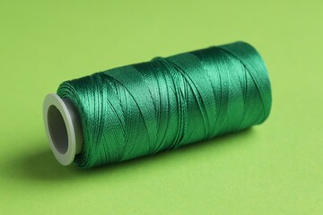 Spool of sewing thread on green background, closeup