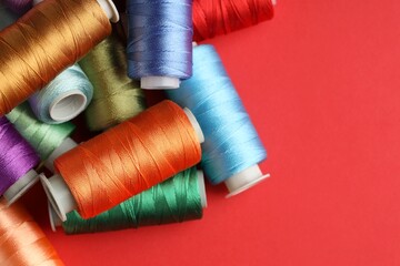 Different spools of sewing threads on red background, flat lay. Space for text