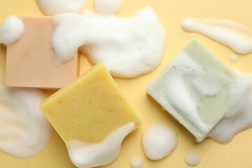 Soap bars with foam on yellow background, flat lay