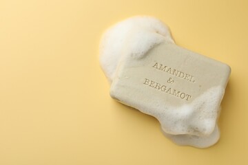 Soap bar with foam on yellow background, top view. Space for text