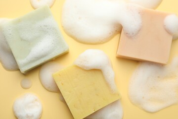 Soap bars with foam on yellow background, flat lay