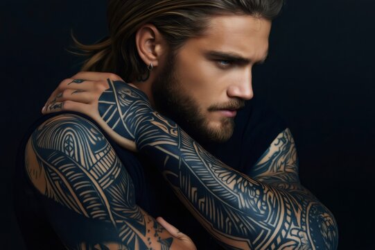 Tattooed model with long hair and a beard, displaying an intricate full sleeve of blackwork tattoo art, exuding individuality and style