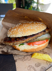 Delicious hamburger with grilled patty, vegetables, and french fries on paper wrapper