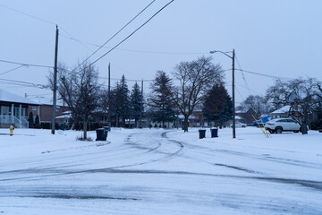 A quiet, snow-covered street in America is captured during a peaceful winter day. The absence of people and the serene atmosphere create a picturesque and tranquil scene.