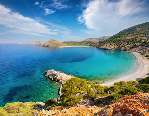 Fototapeta premium A breathtaking coastal view shows vibrant blue Mediterranean waters meeting rugged cliffs and green hills under a bright blue sky with scattered clouds. 
