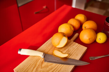 Fresh oranges on a wooden board with a knife in a red kitchen