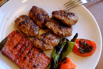 Close-up of sausages and meatballs cooked on a barbecue on a menu plate at a meat restaurant. Portion of meatballs with roasted tomatoes and green peppers. Meat prices. Food industry.
