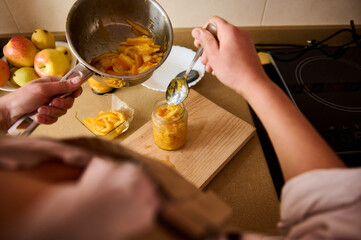 Person prepares orange marmalade by handcrafting jars in a cozy kitchen setting