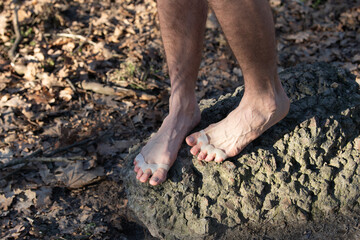 A pair of feet with silicone separators between the toes are positioned on a rocky surface, surrounded by natural elements, showcasing a blend of comfort and nature