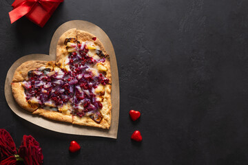 Food for Valentine's Day. Heart shaped sweet pizza with pineapple on black background. Romantic dinner with red wine and gift. View from above. Copy space.