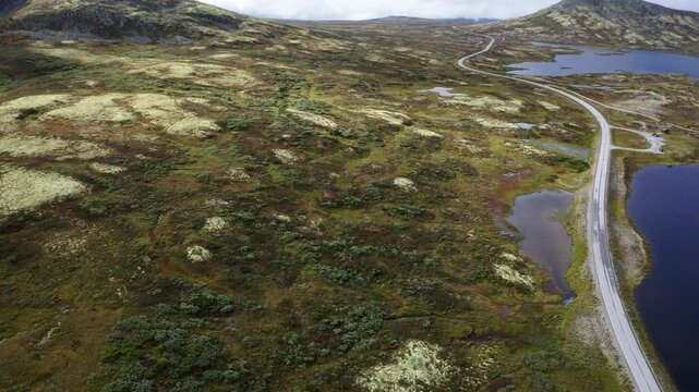 Road leading throught Norvegian severe Tundra nature with birdseye top view. Picturesque northern Norway landscape and modern highway construction aerial 4K video. Rondane National Park, Norway.