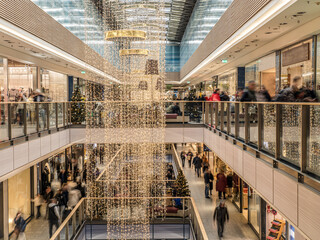 A bustling shopping mall adorned with holiday lights and decorations, filled with customers enjoying the festive ambiance while browsing the variety of retail stores