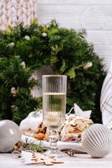 A tall champagne glass filled with sparkling wine stands as the centerpiece on a Christmas table surrounded by stollen bread, pinecones, ornaments, and festive greenery.