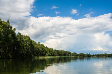 beautiful lake landscape with blue sky and clouds and a row of trees on the horizon