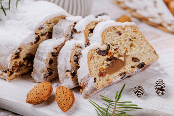 Close-up of Christmas stollen bread sliced on a wooden board, adorned with almonds, festive ornaments, and seasonal decorations.