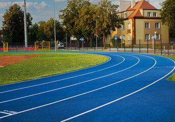A new soccer stadium with artificial green grass, a new blue jogging track with a rubber coating around it, all located in the center of a cozy little European town with minimalist architecture.