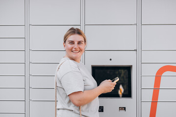 Parcel delivery machine. Mail delivery and post service concept. Happy smiling woman with phone at...