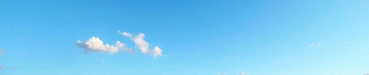 A few wispy clouds dot the bright blue expanse of a clear morning sky, refined, ethereal