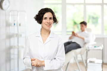 Friendly young female medical person standing in treatment room of medical center