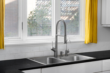 A modern kitchen features a double basin stainless steel sink with a stainless steel faucet, subway tile backsplash, black granite countertop, and yellow curtains.
