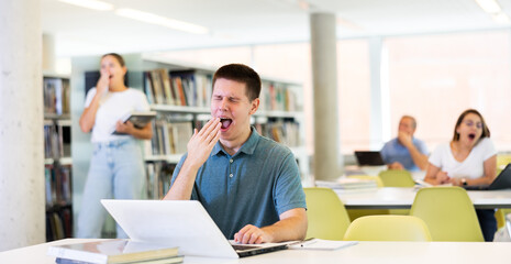 View on bored young male student with a laptop in the school library