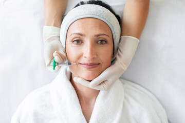 Lip augmentation and correction procedure. European middle aged woman receiving an injection at...