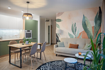 Modern living room with comfortable sofa, carpet on the floor and wallpaper in green leaves on the wall. Contemporary decor of room in stylish interior of apartment. Real estate.	