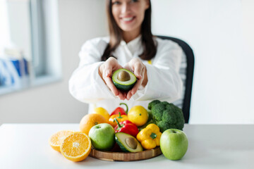Nutritionist, dietitian holding avocado in her hands, promoting healthy vegetables and fruits in...