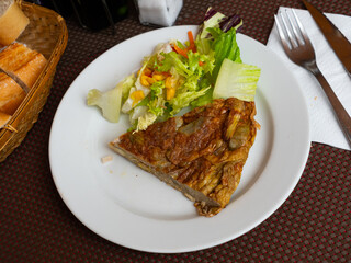 Slice of appetizing artichoke omelette served with colorful fresh vegetable salad and crusty bread. Traditional Spanish dish