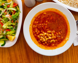 Traditional Turkish Kuru fasulye, spicy stewed bean dish in tomato sauce served with rice and fresh vegetable salad