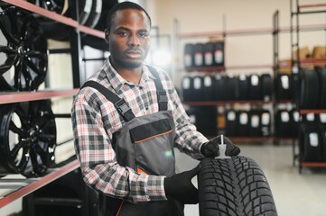 A professional African american worker in a car service measures the tread diameter of a wheel with...