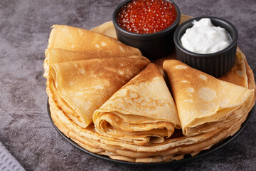 Delicious stack of golden pancakes served with cream and caviar on a rustic table