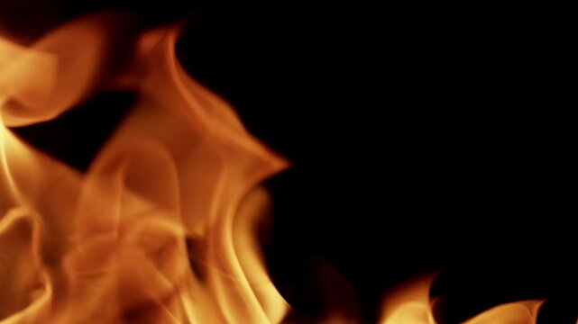 Beautiful dancing fire, the surface is ablaze. Lots of fire. Close-up immersion in the flames. The camera passes through the fire. Burning tongues of flame on a black backdrop in slow motion. 4K.