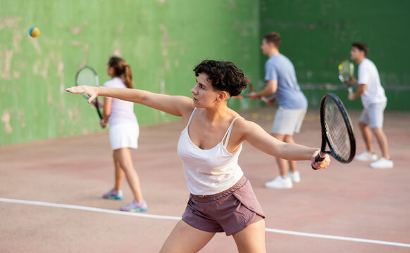 Active fit young hispanic woman playing frontenis on open court on summer day, hitting ball with strung tennis racquet to score to opposing team. Popular Spanish sports..