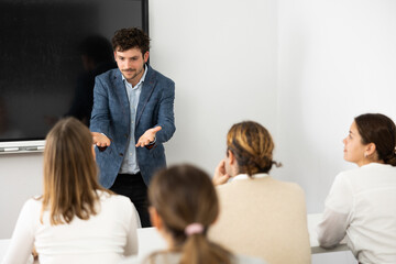Fototapeta premium Positive male trainer, conducting advanced training courses to office employees sitting at desks in auditory