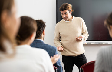 Fototapeta premium Middle-aged man standing near interactive board and communicating with adult students during foreign language class