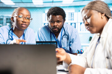 Group of healthcare specialists in scrubs analyzing results with doctor, emphasizing teamwork,...