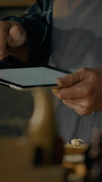 A person focuses on a tablet screen while engaged in a woodworking task. The well-lit workshop features tools and wooden materials scattered around, indicating active craftsmanship