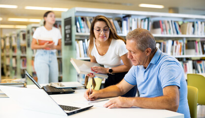 Female Latina college student working on a project with a male elder in the school library