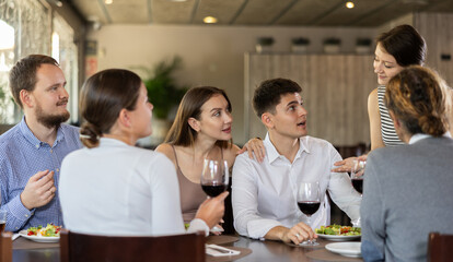 Young woman waitress taking order from group of friends at table in restaurant