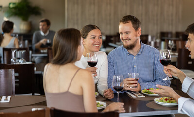 Two couples meet for dinner at restaurant. They chat and drink red wine