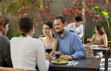 Two couples of men and women drinking eating and talking on restaurant terrace
