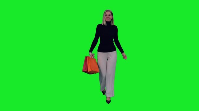 Happy middle aged woman walking with colorful shopping bags on green chroma key background, 4k pre-keyed footage