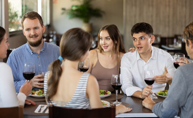 Group of men and women friends eating drinking and talking in restaurant