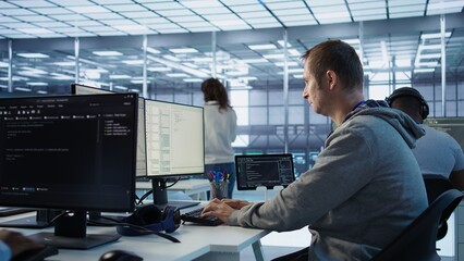Engineer starting job shift in server hub used for processing vast amounts of data. IT programmer arriving at work in data center, sitting at PC desk, typing on keyboard, camera B