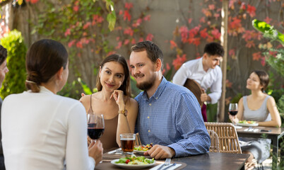 Two couples of men and women drinking eating and talking on restaurant terrace