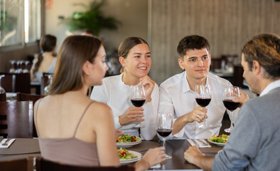Two couples of men and women drinking eating and talking in restaurant