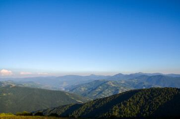 Peaceful panoramic view of rolling hills lush green forests and distant peaks under clear blue sky. Perfect depiction of natural beauty and tranquility in mountainous region. Carpathians, Ukraine